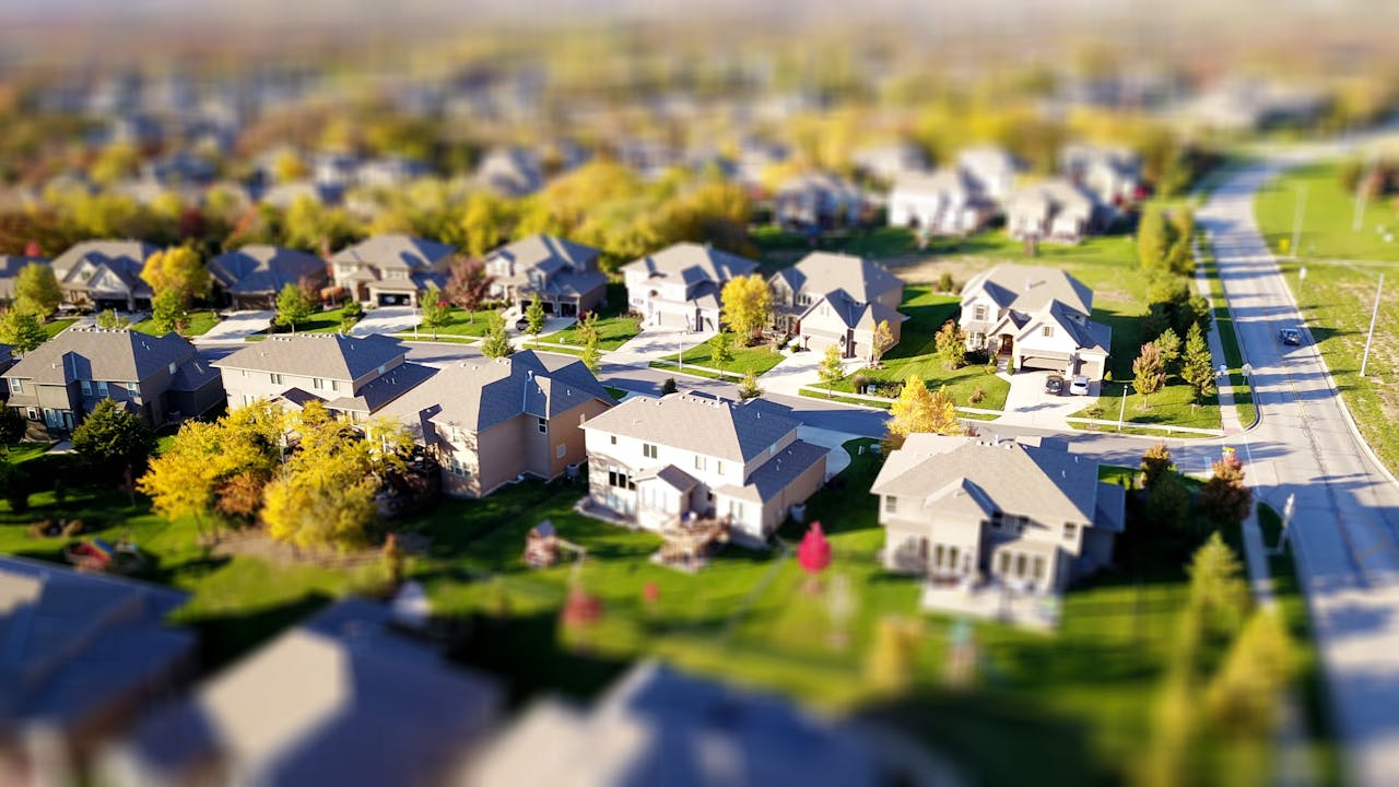 our-services-1 Tilt-shift aerial photo of a suburban neighborhood with green lawns and roads.