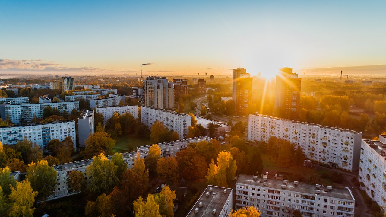 our-services-2 Aerial view of a cityscape at sunrise with autumn foliage and modern buildings.